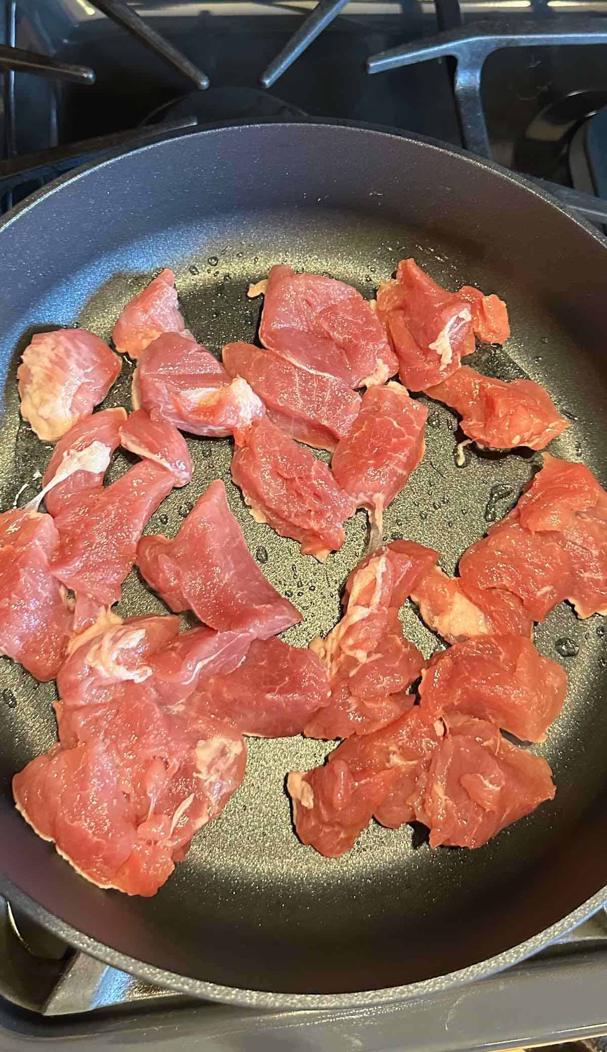 Pork tenderloin slices cooking in oil in a skillet.