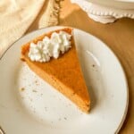 A slice of pumpkin pie on a plate topped with whipped cream.