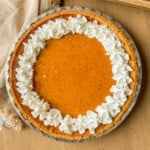 A pumpkin pie with graham cracker crust and topped with whipped cream.