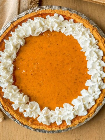 A pumpkin pie with graham cracker crust and topped with whipped cream.