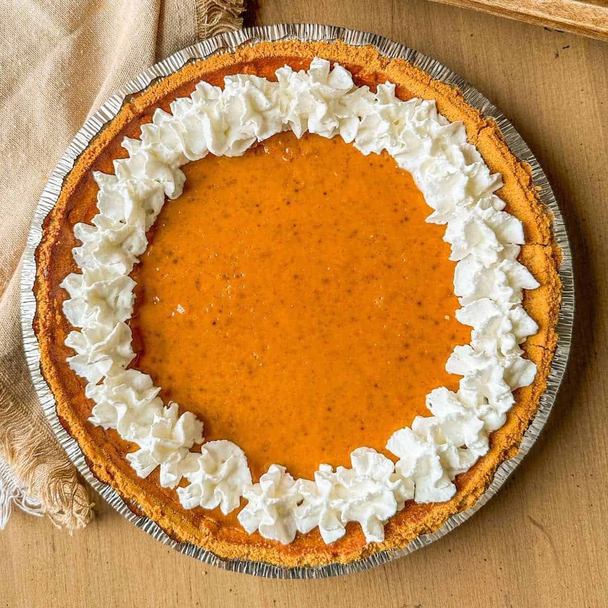 A pumpkin pie with graham cracker crust and topped with whipped cream.
