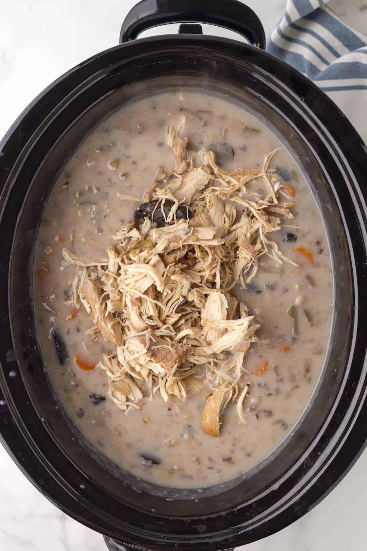 Cooked chicken on top of a wild rice soup in the slow cooker.