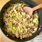 A skillet with ground pork and shredded cabbage and a wooden serving spoon.