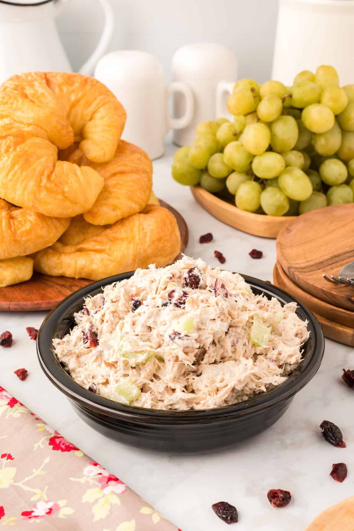 A bowl of cranberry walnut chicken salad with croissants and grapes in the background.