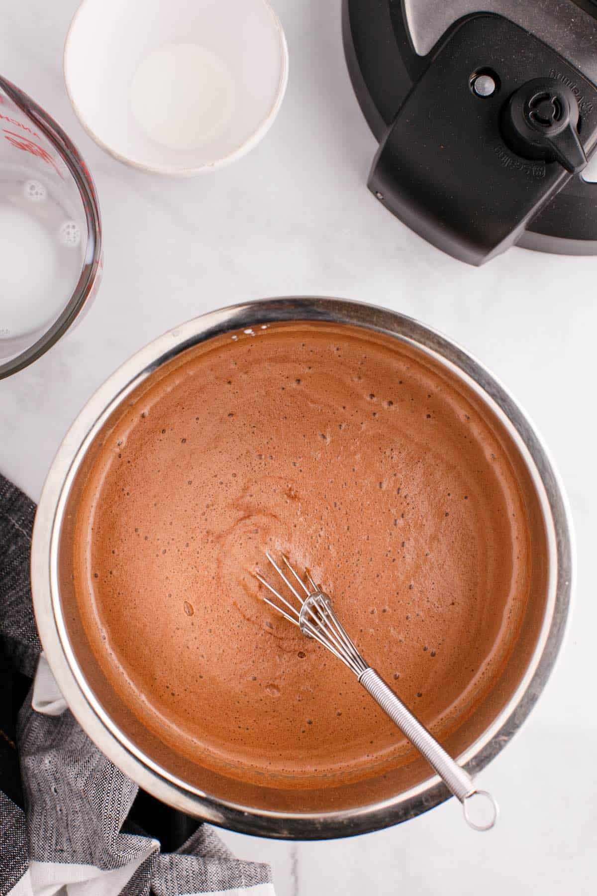 A pot of creamy hot chocolate in an instant pot insert with a whisk.
