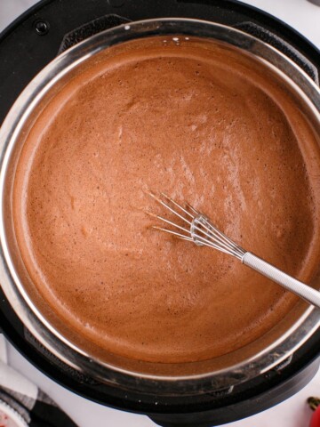 A pot of creamy hot chocolate with a metal whisk.
