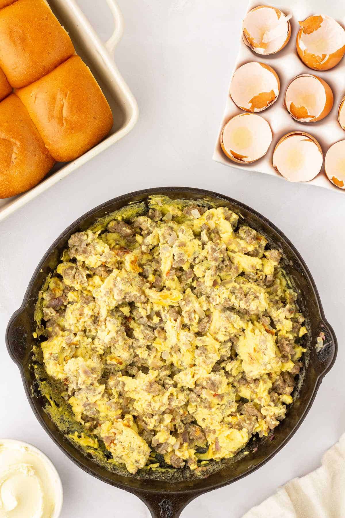 Scrambled eggs and pork sausage in a cast iron skillet.