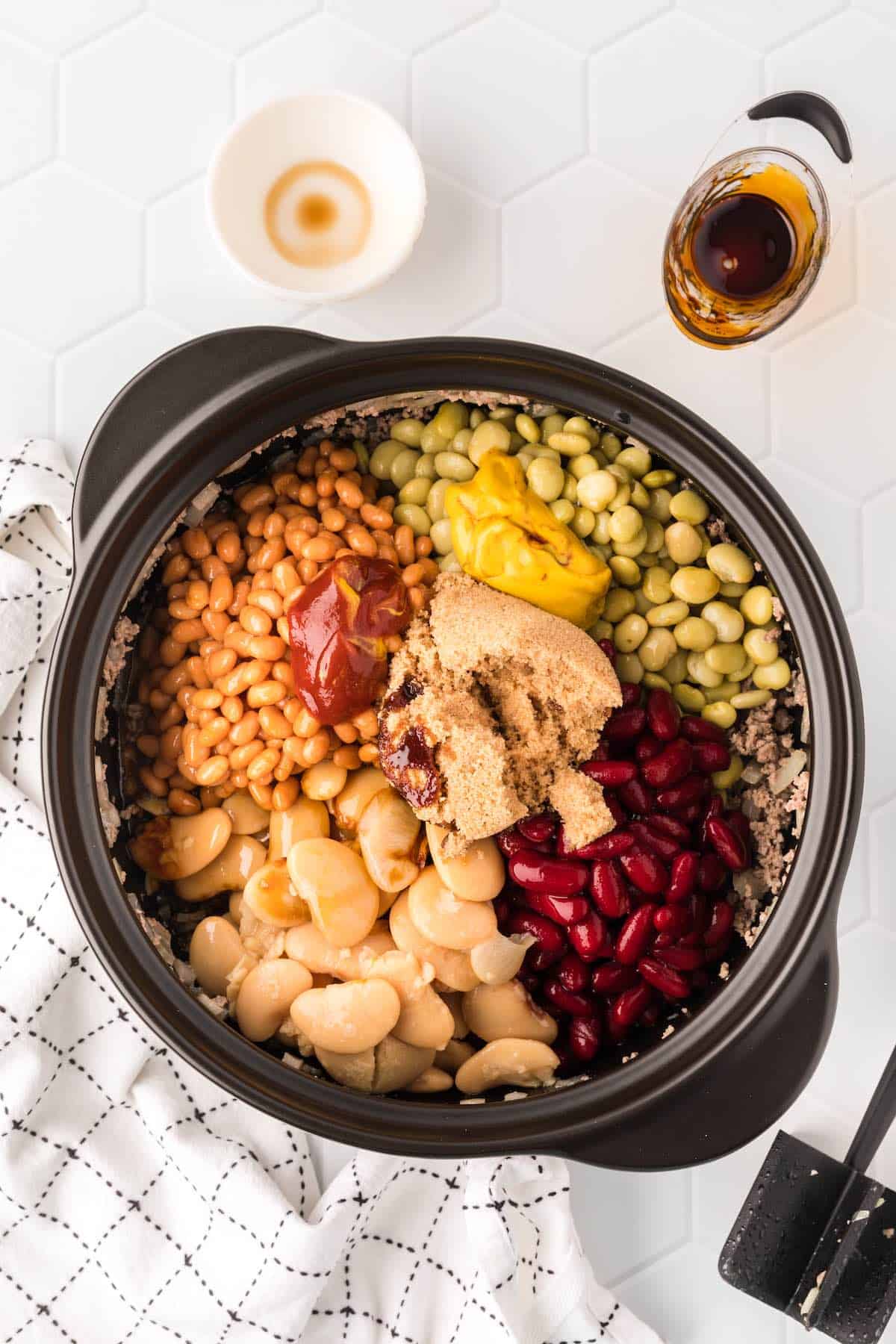Beans, brown sugar and seasonings on top of the cooked ground beef in a large pot.