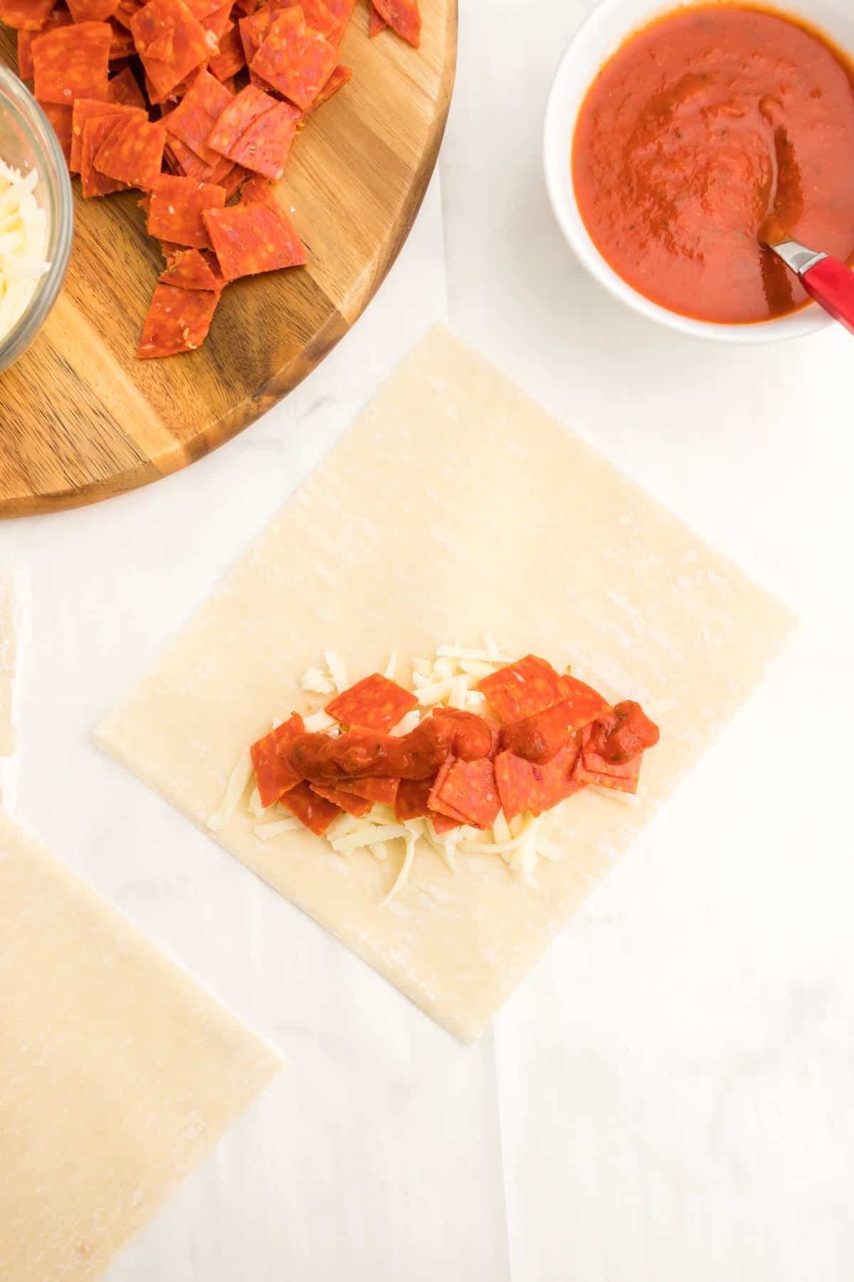 An egg roll wrapped laid out and topped with pepperoni and cheese.