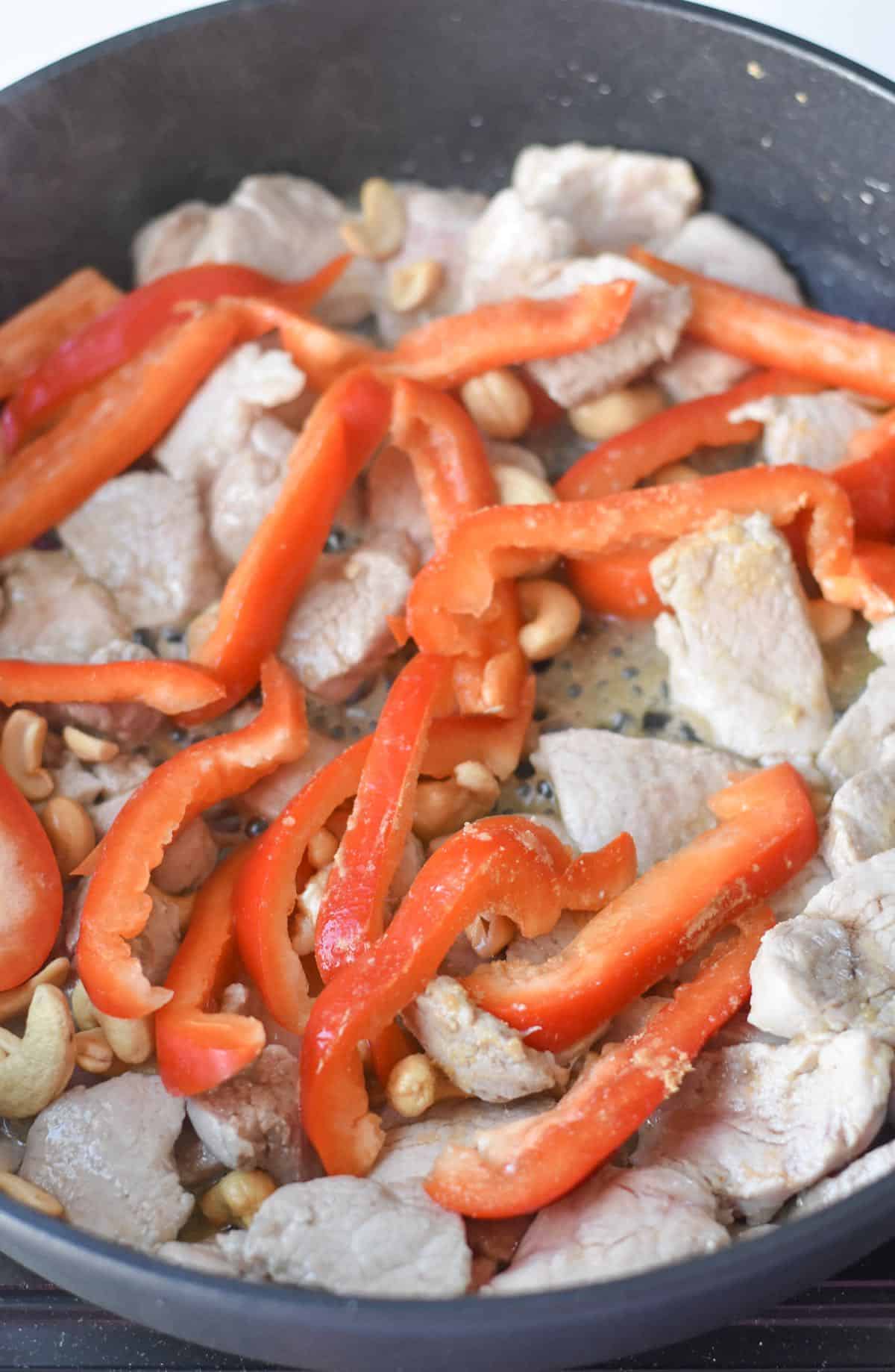 Pork tenderloin in a skillet with sliced red bell peppers.