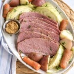 Sliced corned beef on a platter with cabbage, potatoes and carrots.