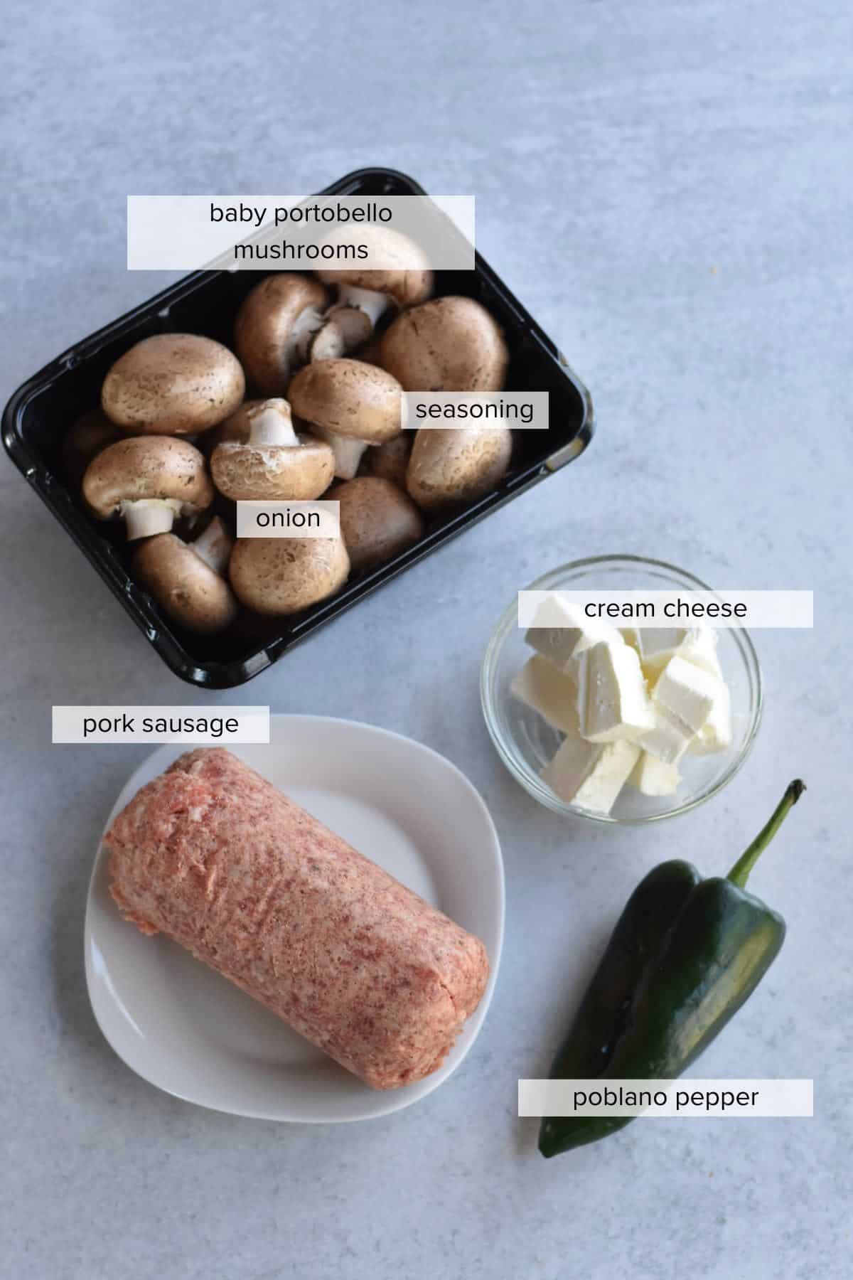 Four ingredients on a countertop include mushrooms, pork sausage, cream cheese and a pepper.