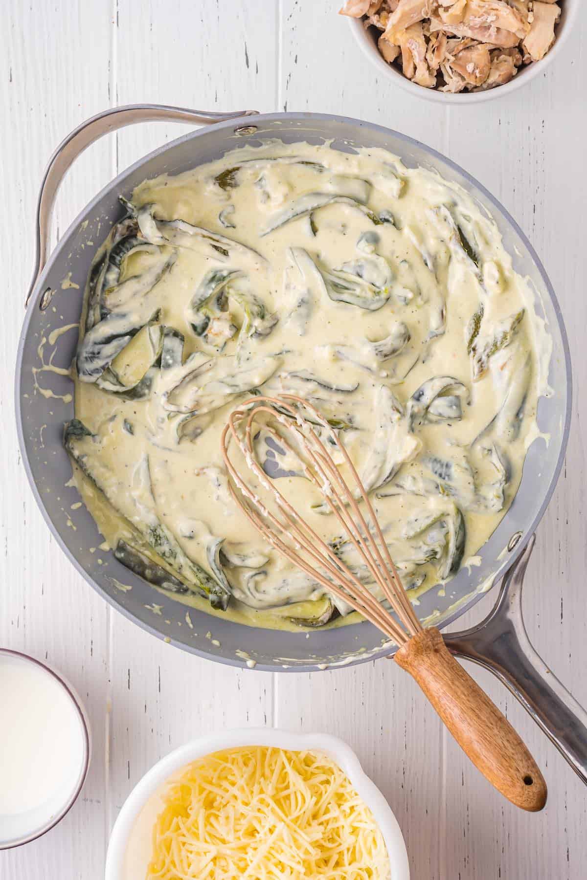 A creamy cheese sauce with poblano peppers and a whisk.