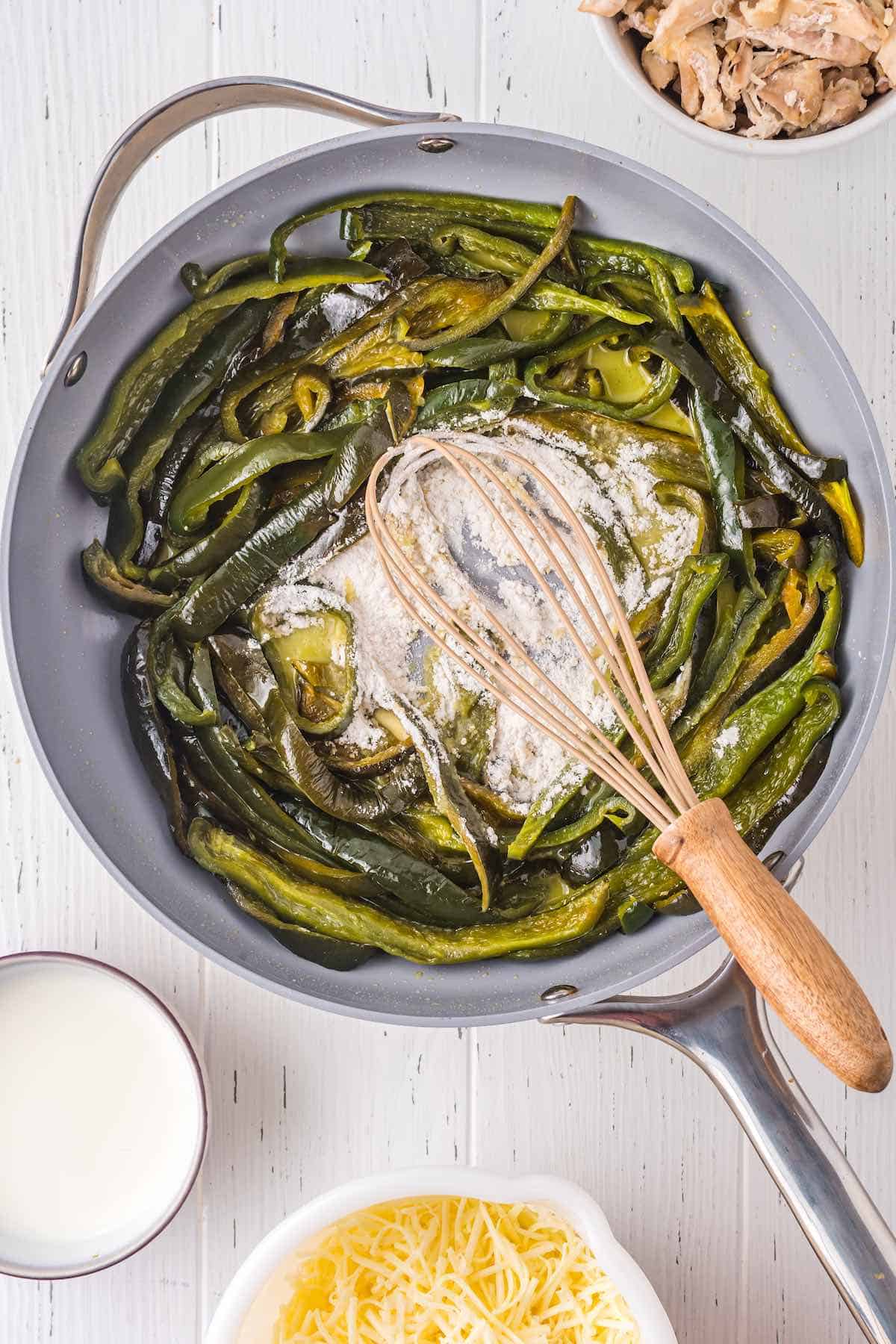 Sauteed poblano peppers in a skillet with flour and a whisk.