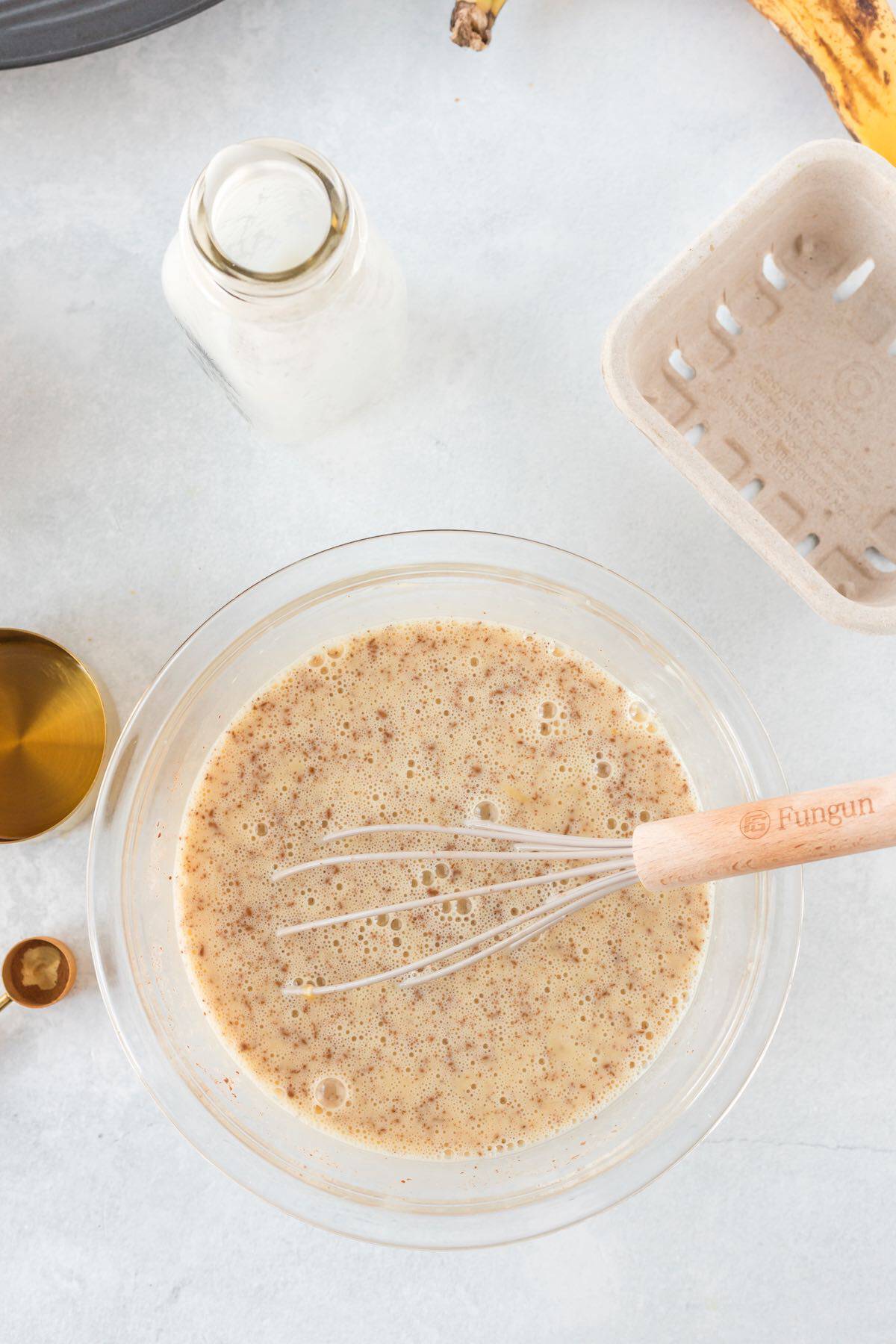 Eggs, milk and cinnamon custard mixture in a bowl with a whisk.