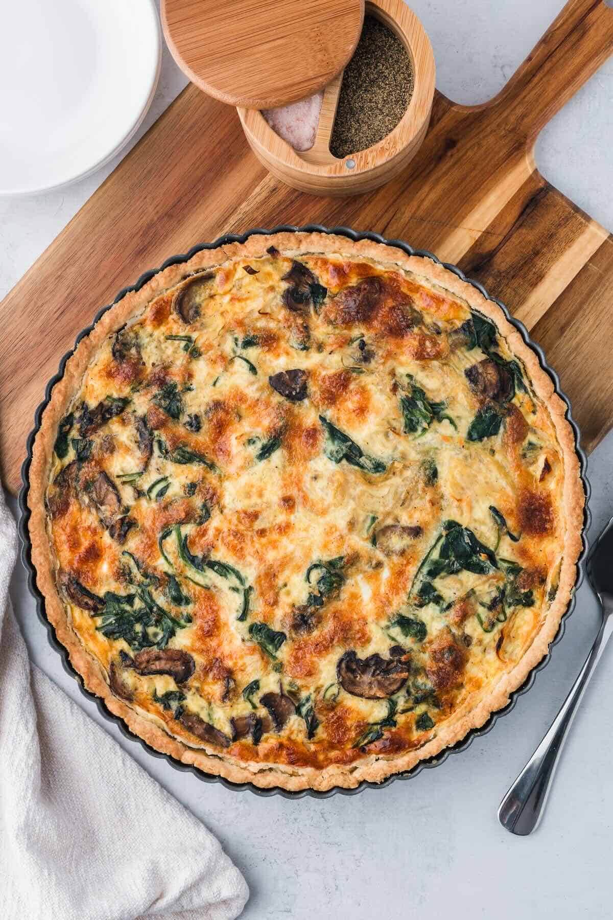 A baked quiche with spinach and mushrooms in a tart pan.