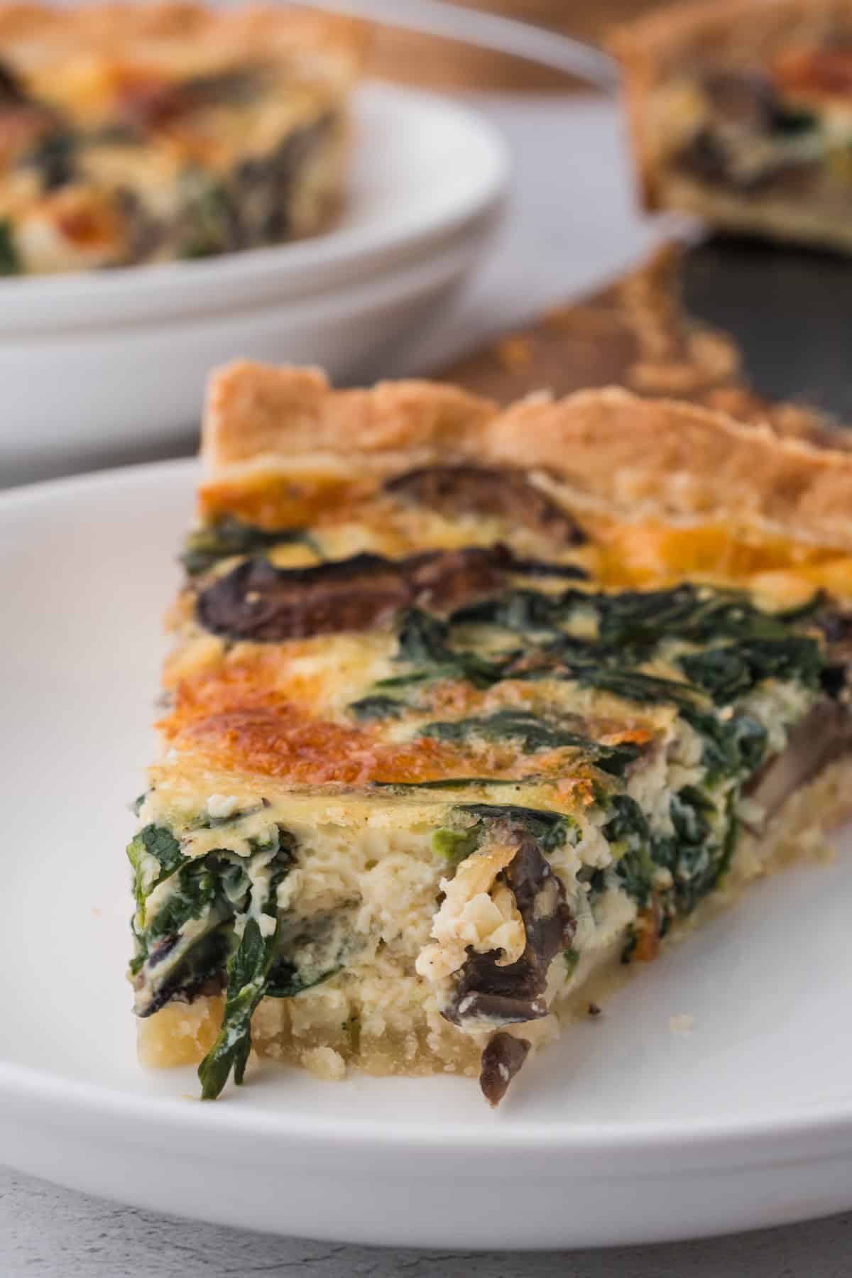 A slice of a spinach quiche with mushrooms.