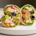 Chicken wraps with pesto and black olives, cut in half on a plate.
