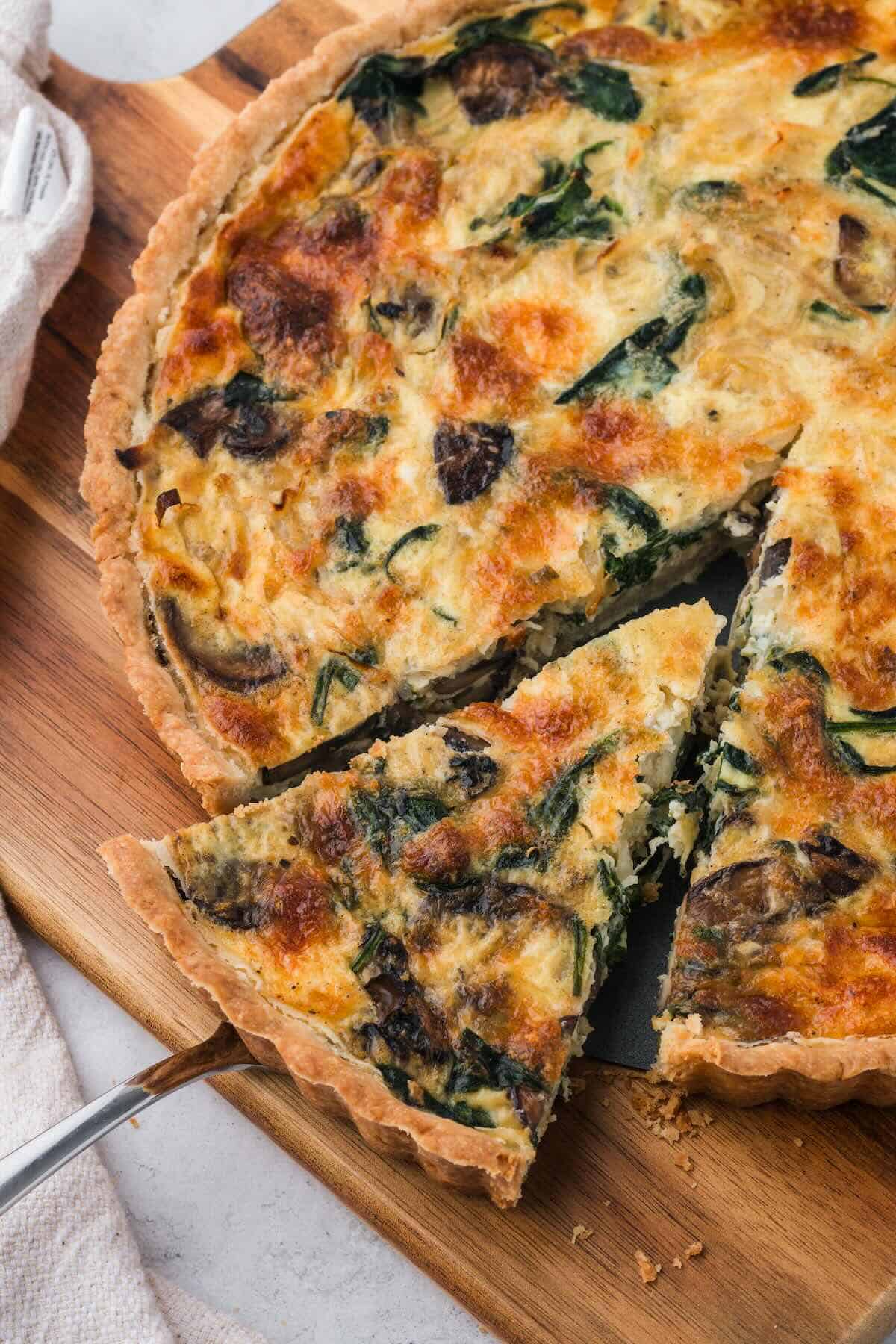 A sliced spinach and mushroom quiche on a cutting board.