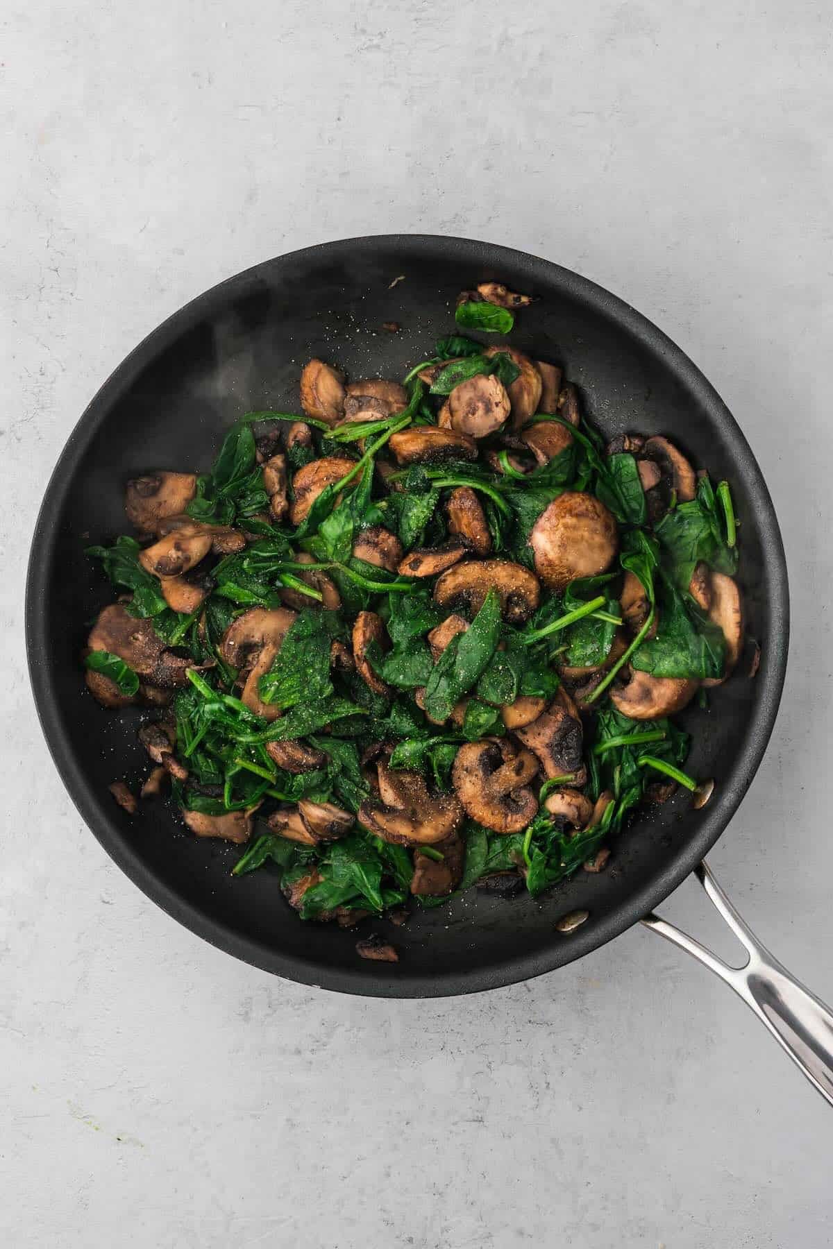 Cooked mushrooms and wilted spinach in a pan.