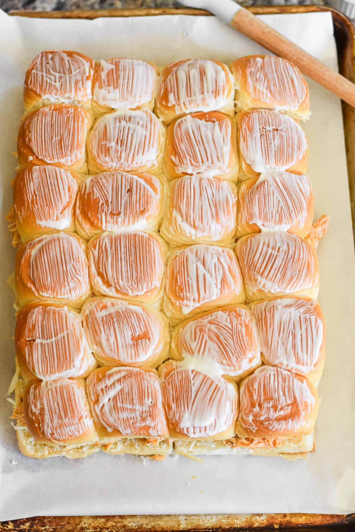 Ranch dressing brushed onto the top of buffalo chicken sliders.