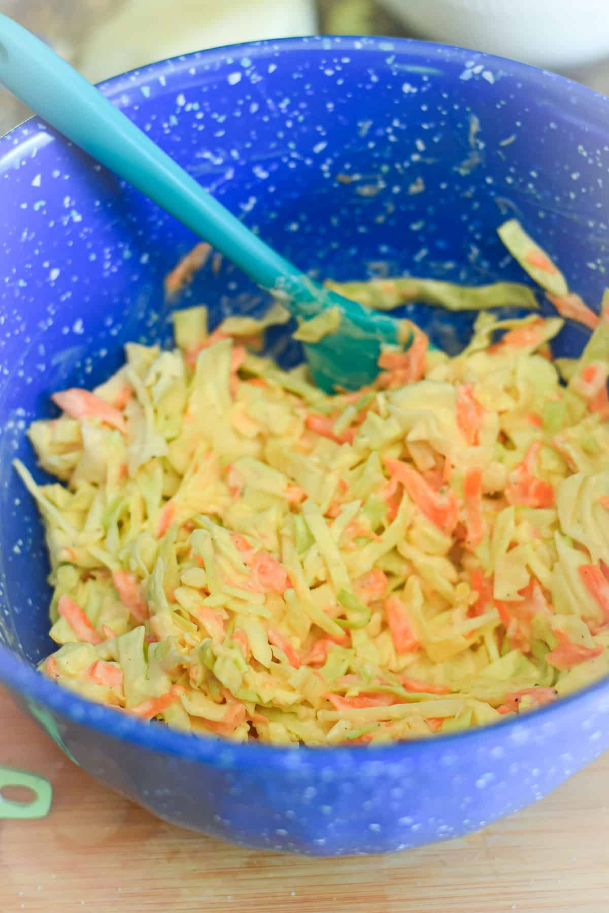 Tossed sweet coleslaw in a bowl with a spatula.