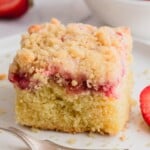 A slice of yellow cake with strawberries and a crumb topping.