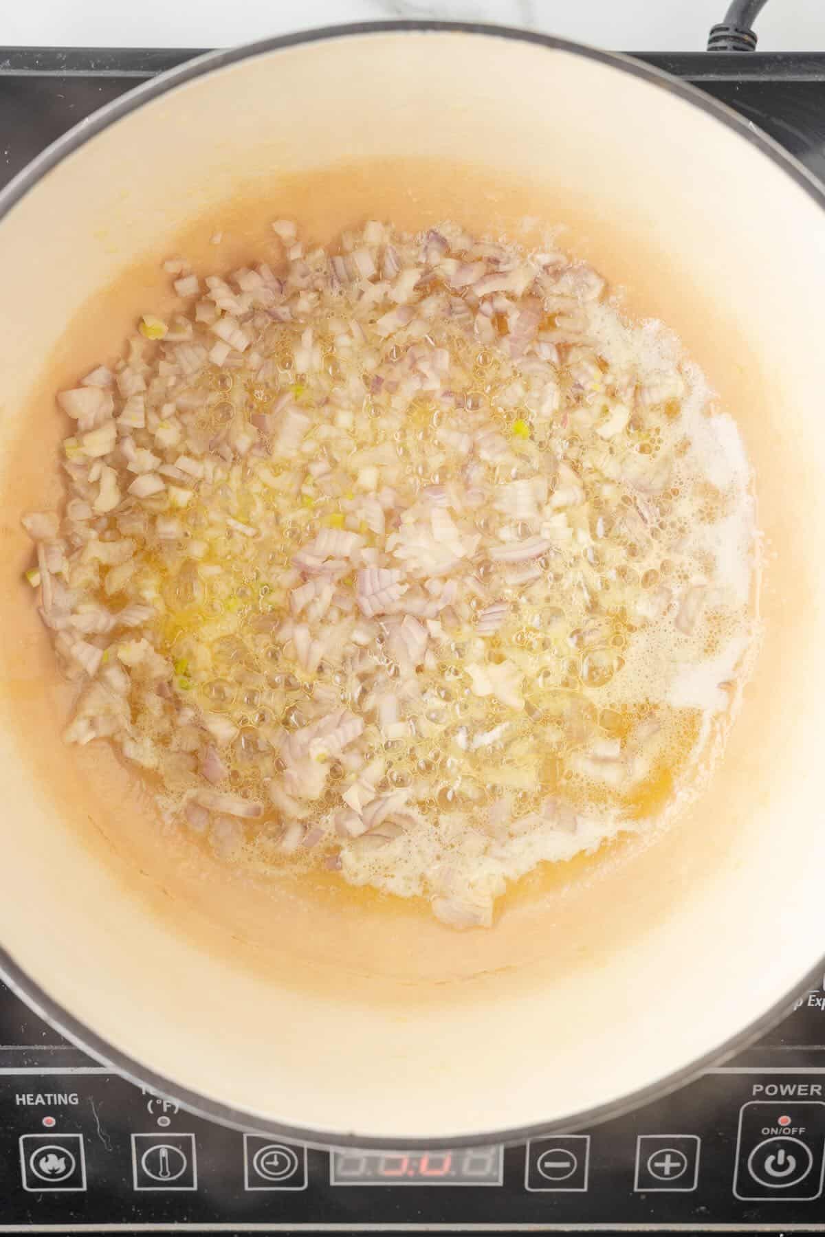 A Dutch oven with butter, oil, cooked shallot and garlic.