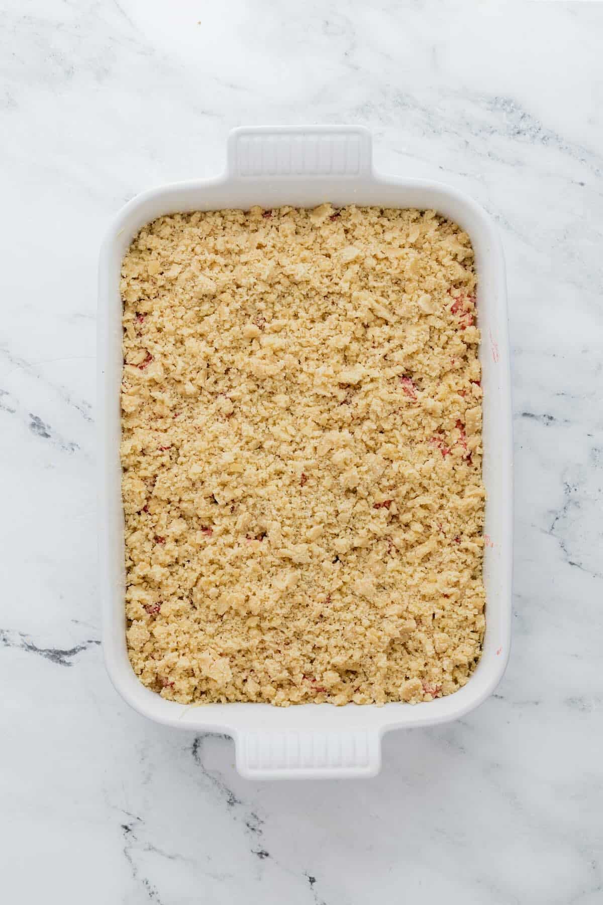An unbaked strawberry cake topped with crumb topping in a rectangle pan.