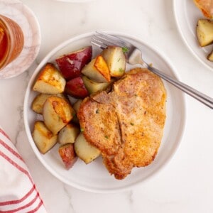 Bone in pork chops on a plate with seasoned potato pieces.