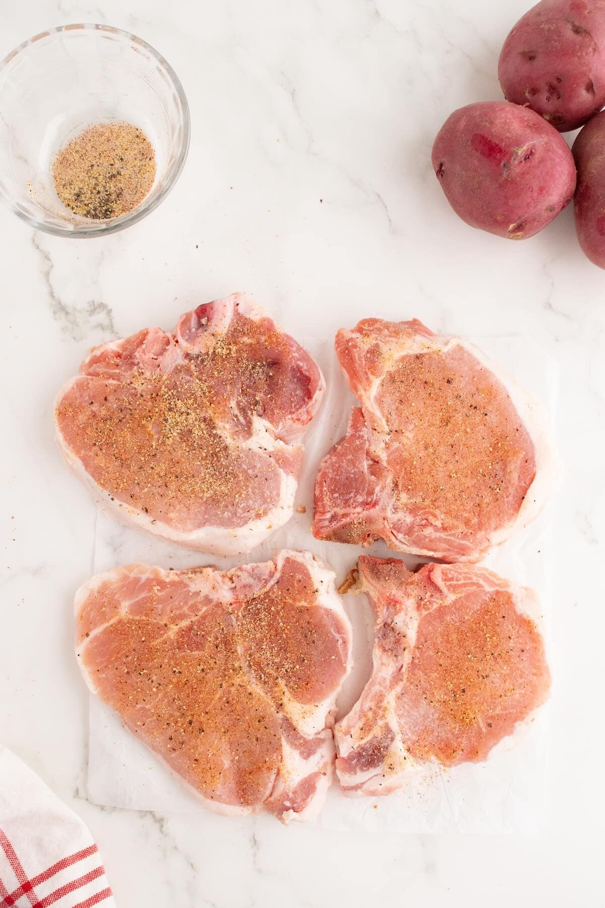 Pork chops sprinkled with seasoning blend on a plate.