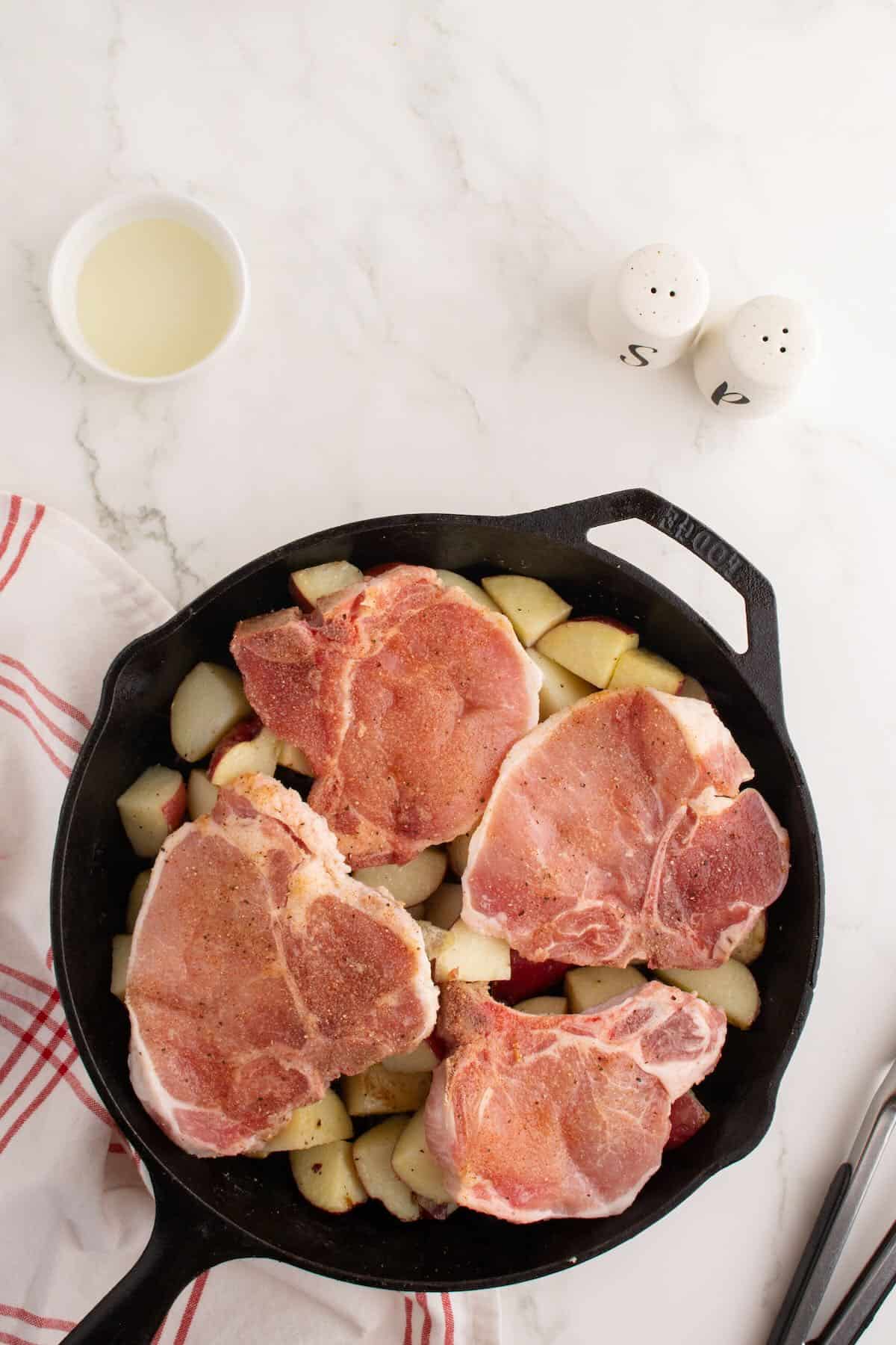 Pork chops resting on potato pieces in a skillet.