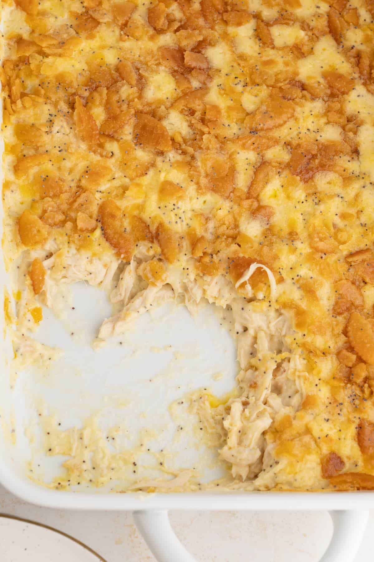 Creamy poppy seed chicken casserole baked in a white casserole dish with a golden buttery Ritz cracker topping.