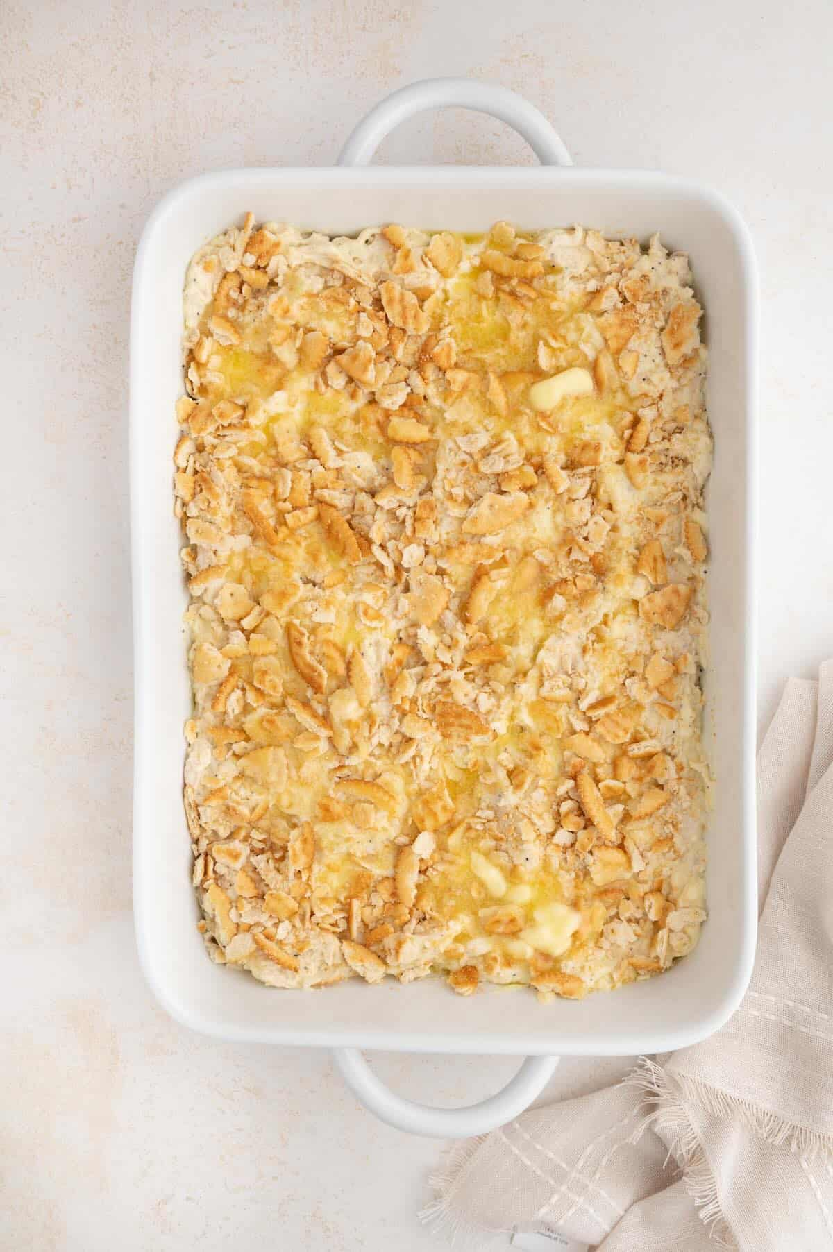 Crushed buttery crackers mixed with melted butter being sprinkled over poppy seed chicken casserole.