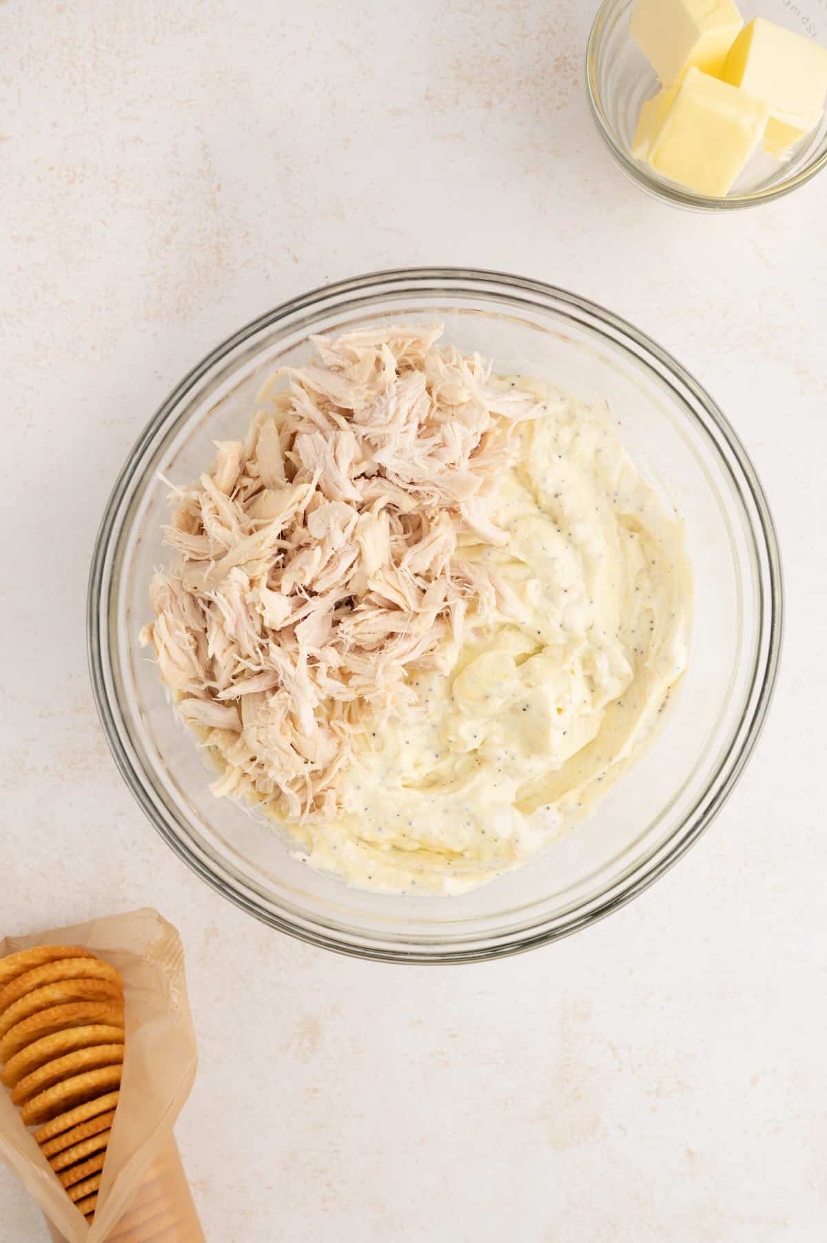 Pouring shredded chicken into a creamy poppy seed sauce before baking the casserole.