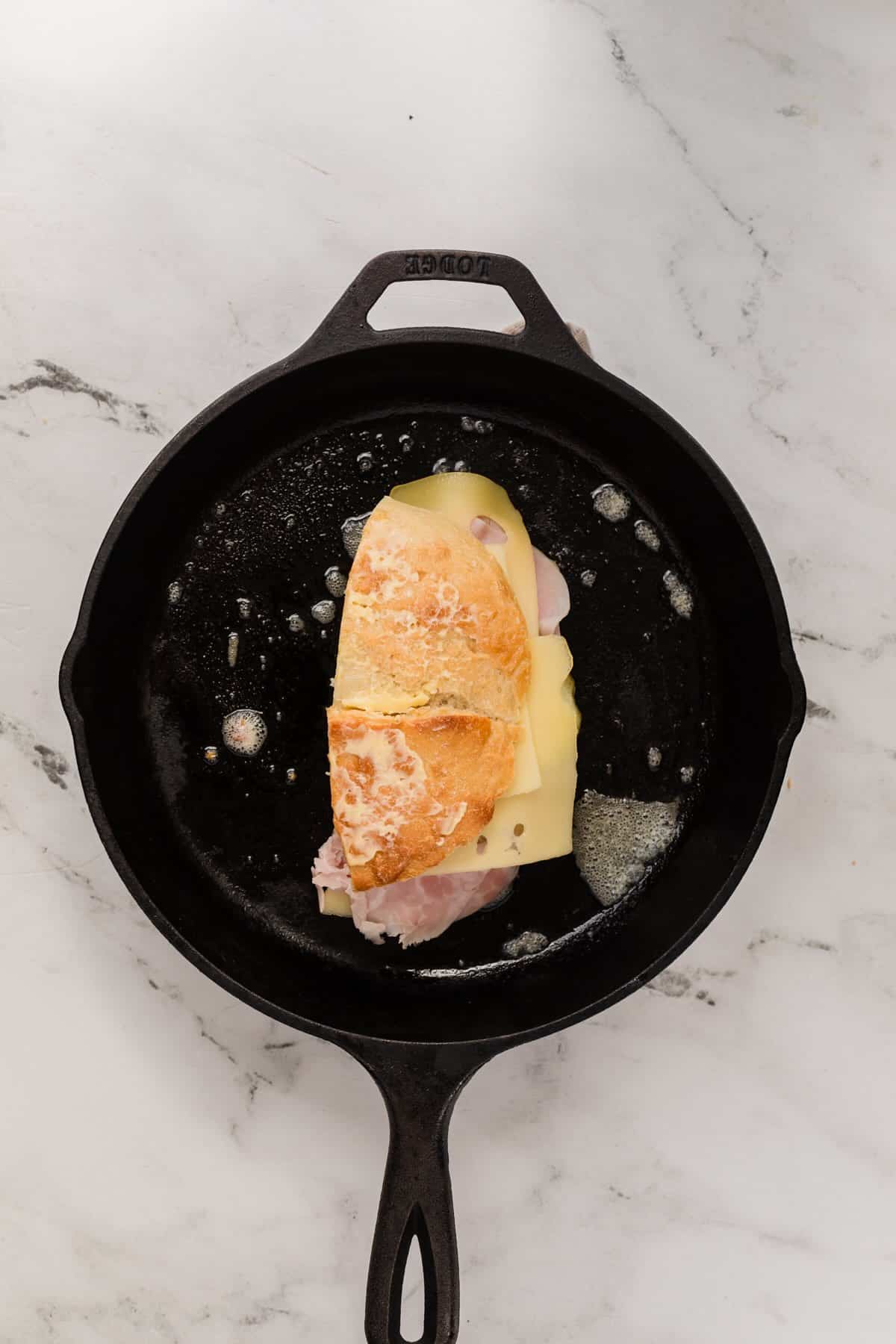 A cast iron skillet heating a pork and ham sandwich.