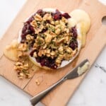 Baked brie with cranberries and walnuts served on a wooden board with crackers and fresh rosemary.