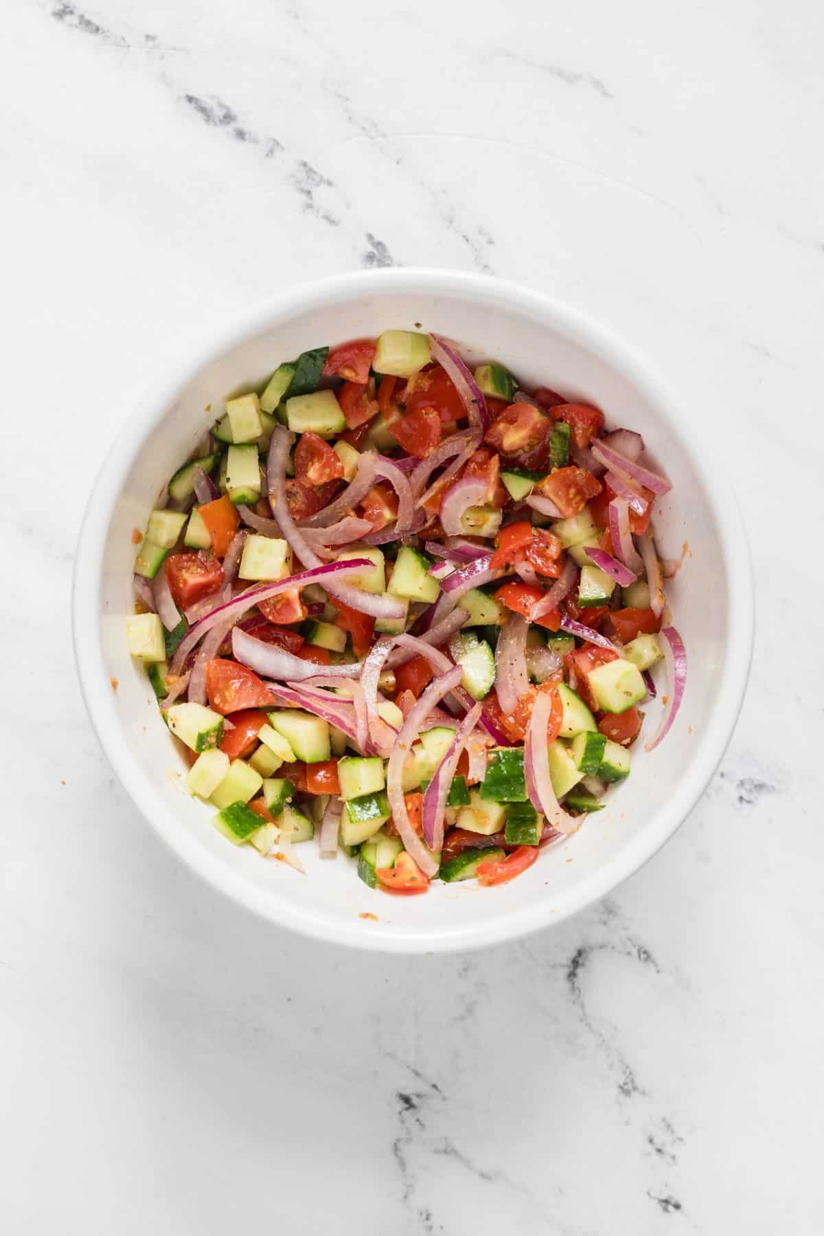Cucumbers, tomatoes, red onions and spices marinating in a bowl.