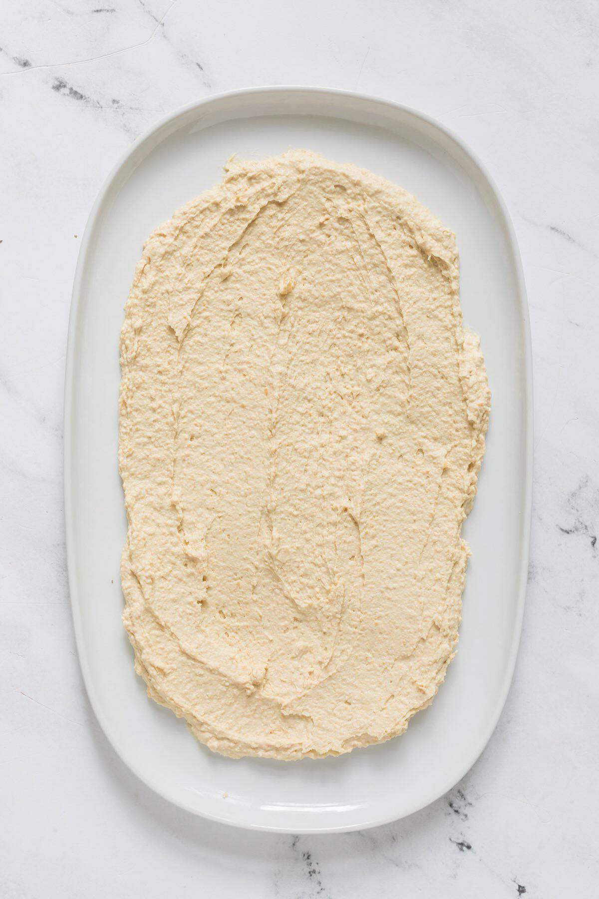 Hummus spread in a layer on a platter,.