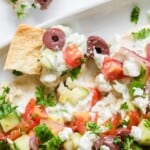 A layered hummus dip with feta cheese and olives and pita chips.