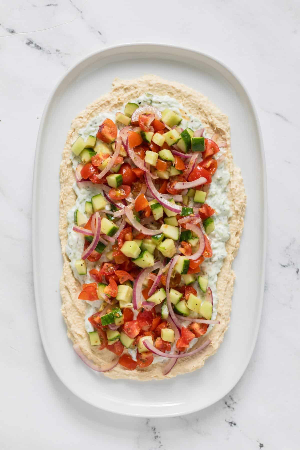 Mediterranean vegetable dip on top of hummus and tzatziki.