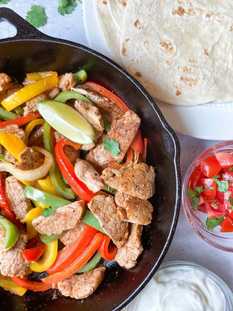 Pork fajitas sliced in a cast iron pan with bell peppers.