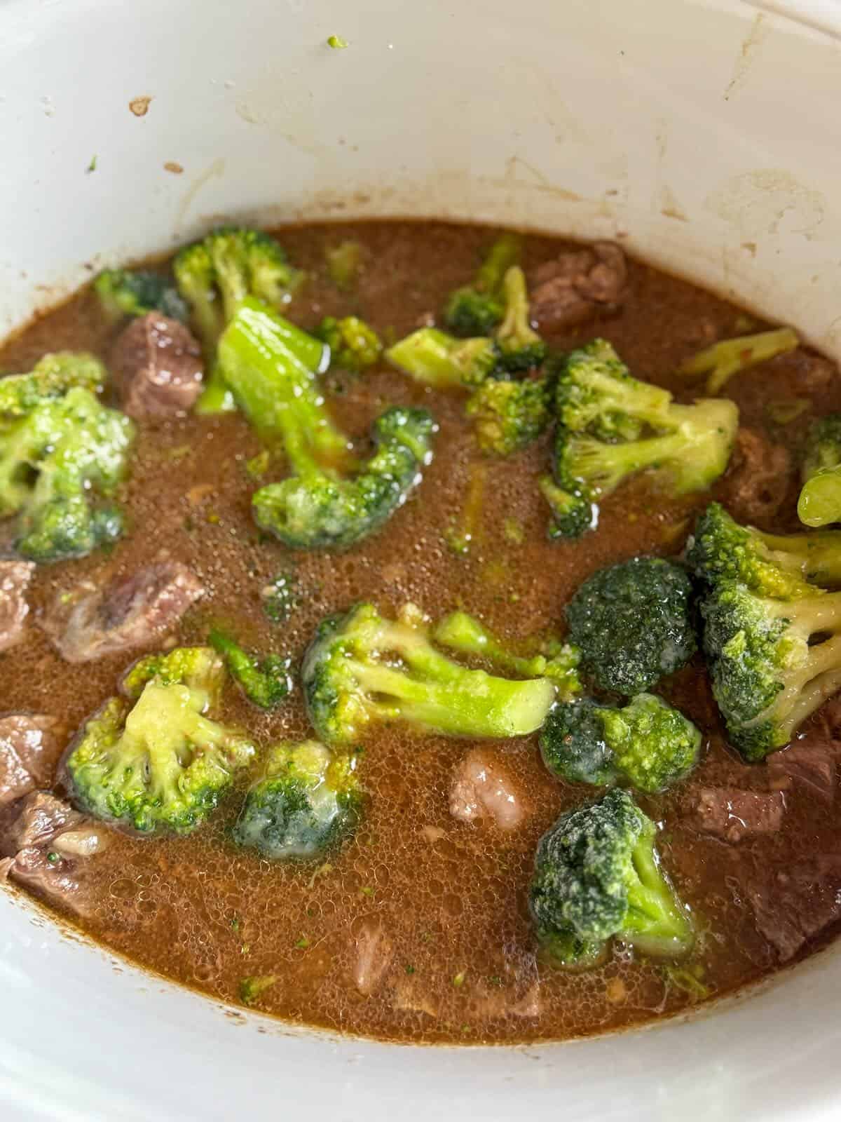Frozen broccoli florets added to tender beef in a slow cooker.