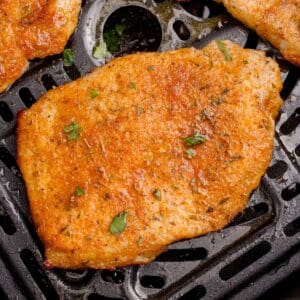 A cooked and seasoned thin pork chop in the air fryer basket.