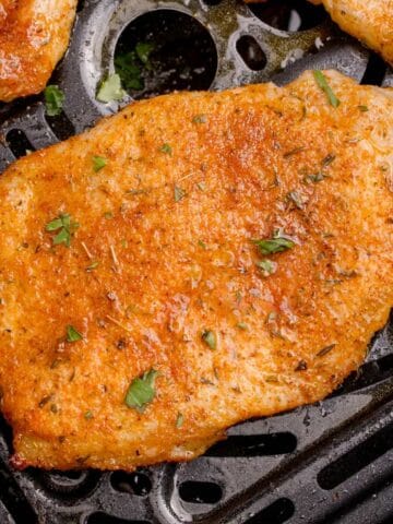 A cooked and seasoned thin pork chop in the air fryer basket.