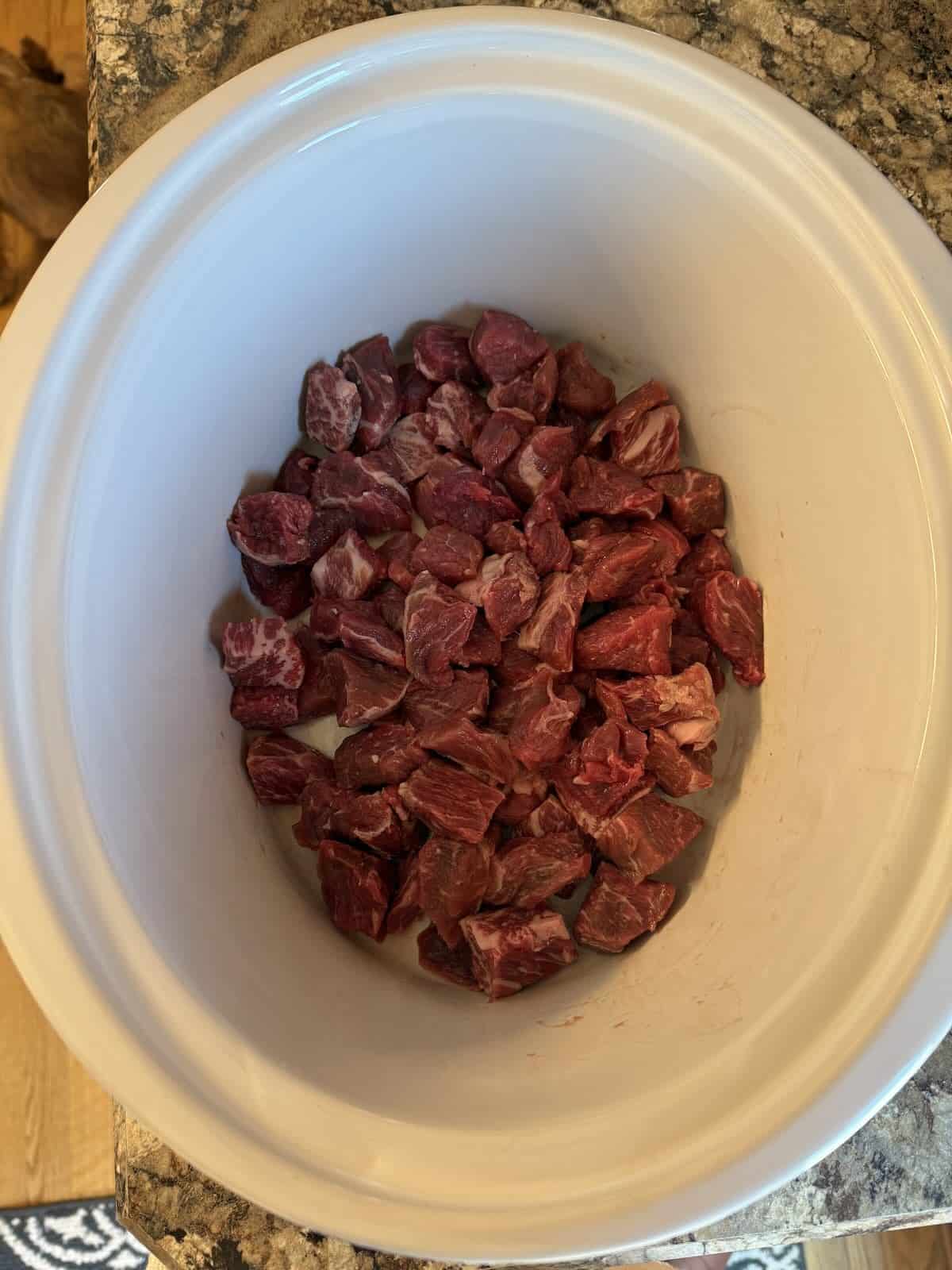 Raw beef chunks in a slow cooker.
