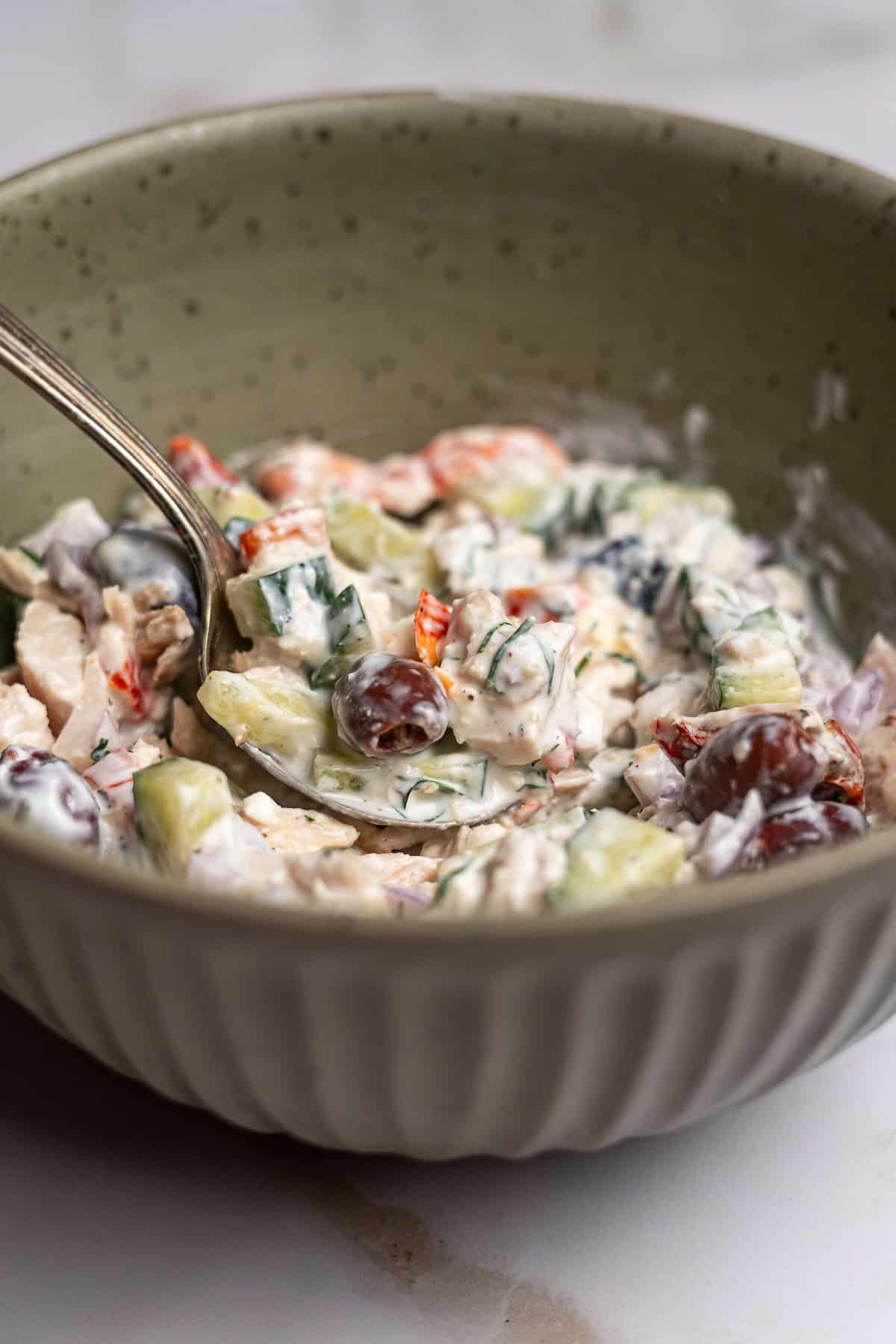 A spoonful of creamy tuna salad with olives and cucumbers.