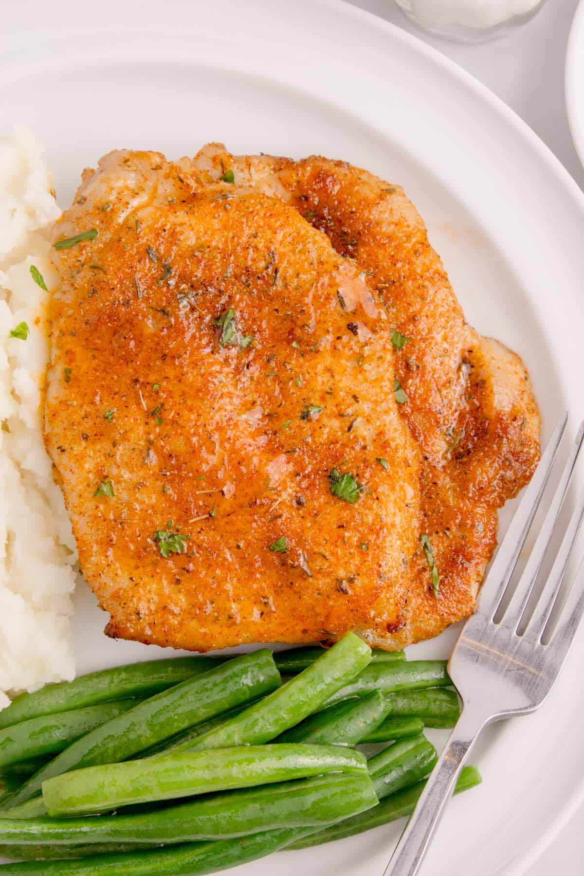 Golden-brown thin pork chops cooked in the air fryer, served on a plate with mashed potatoes and green beans.