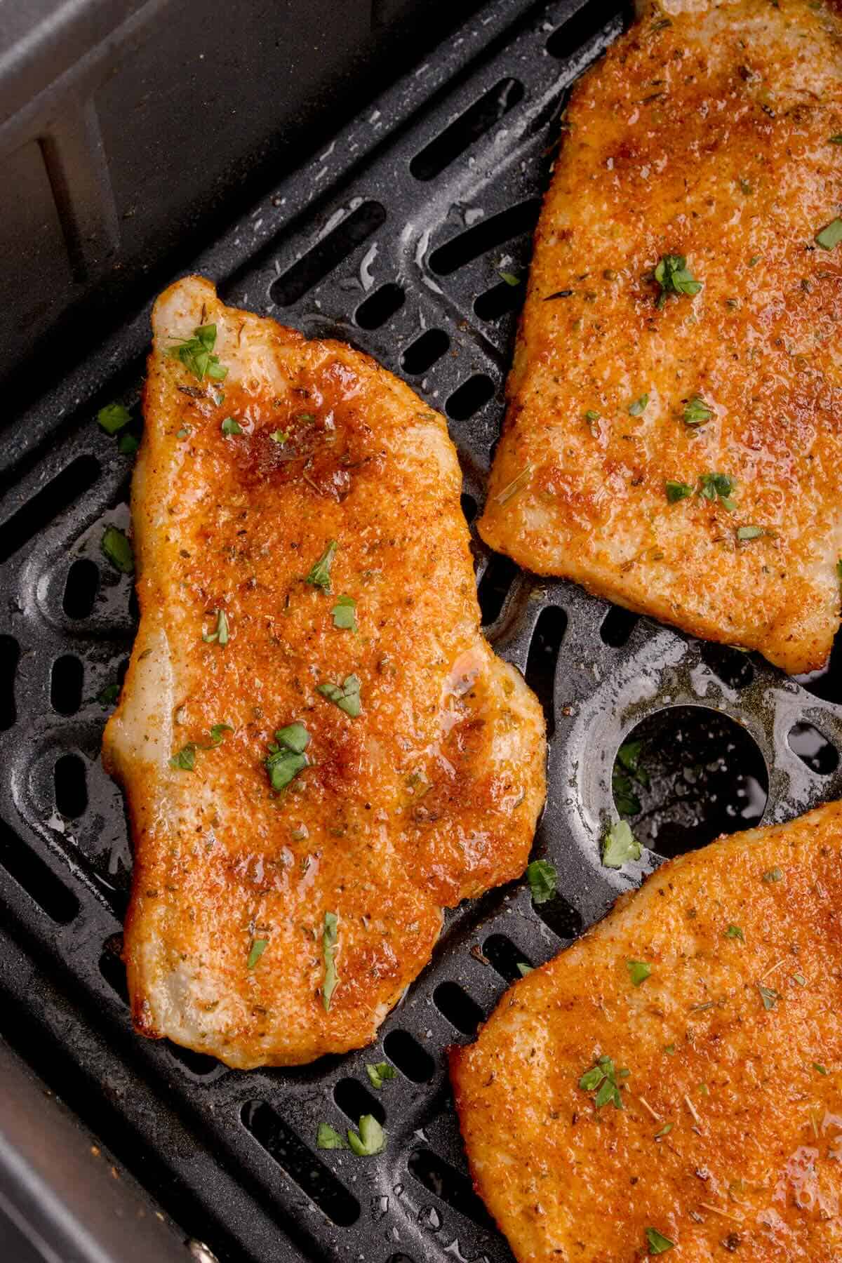 Cooked pork chop in the air fryer, sprinkled with fresh parsley.