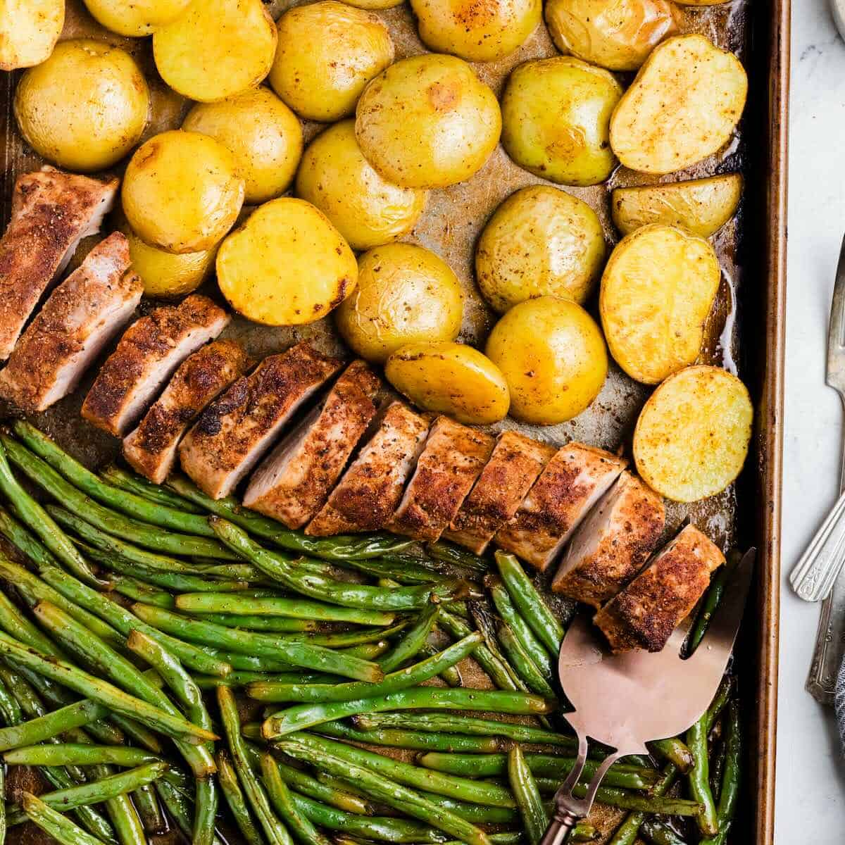 Flavorful pork tenderloin and roasted vegetables on a baking sheet, fresh out of the oven.
